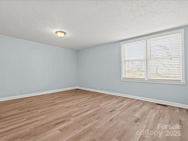 unfurnished room featuring light wood-type flooring, visible vents, a textured ceiling, and baseboards