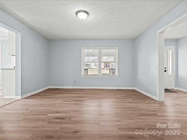 empty room with a textured ceiling, baseboards, and wood finished floors