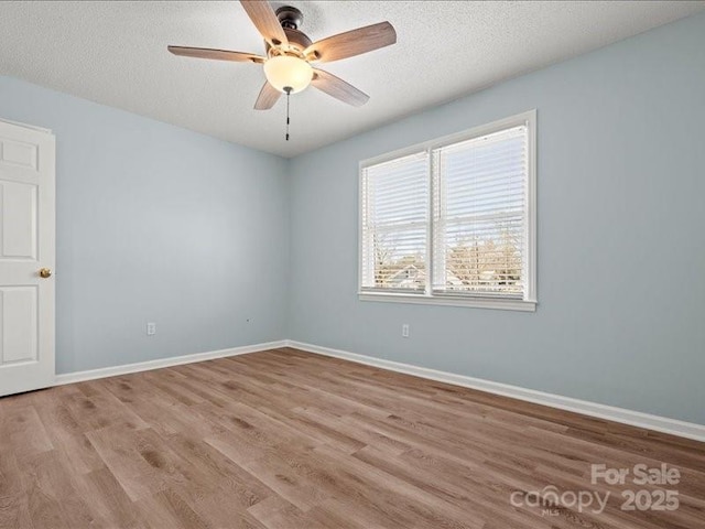 spare room with light wood-type flooring, ceiling fan, a textured ceiling, and baseboards