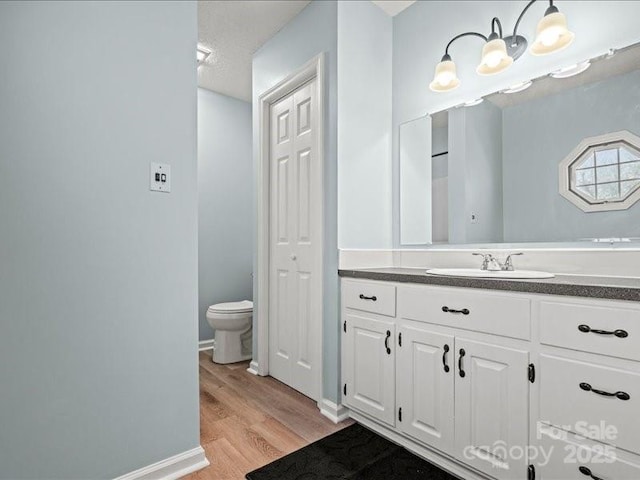 bathroom with baseboards, vanity, toilet, and wood finished floors