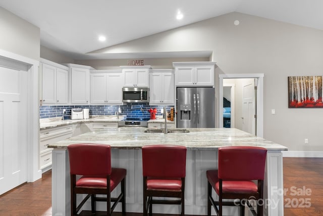 kitchen with a sink, white cabinetry, appliances with stainless steel finishes, and vaulted ceiling