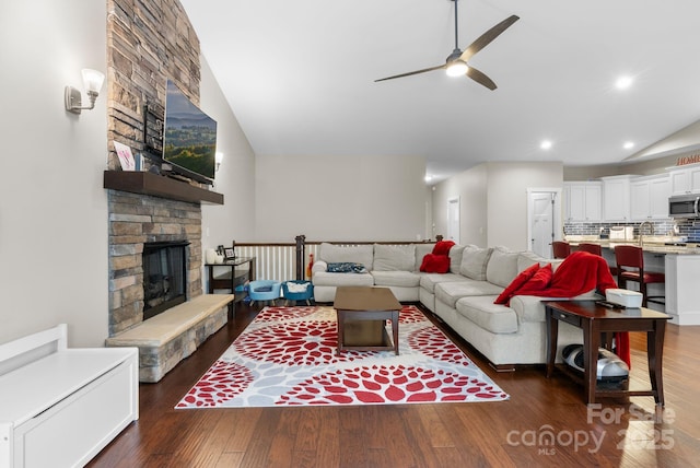 living room featuring a fireplace, vaulted ceiling, wood finished floors, and a ceiling fan