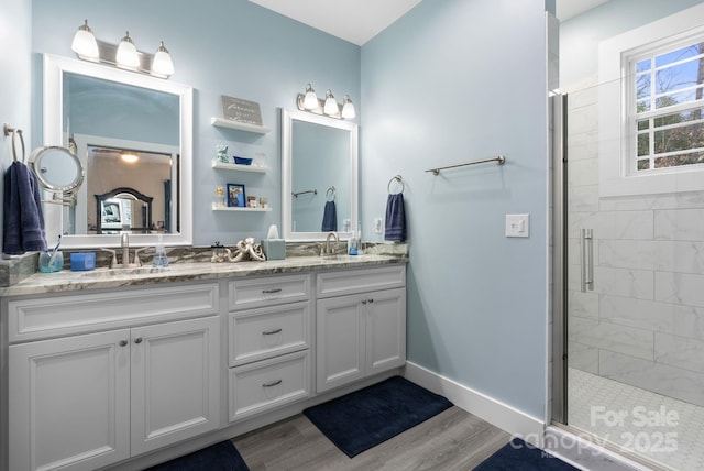 bathroom with wood finished floors, baseboards, double vanity, a stall shower, and a sink