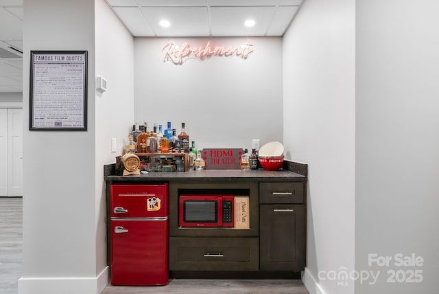 bar with white microwave, a bar, a paneled ceiling, and wood finished floors