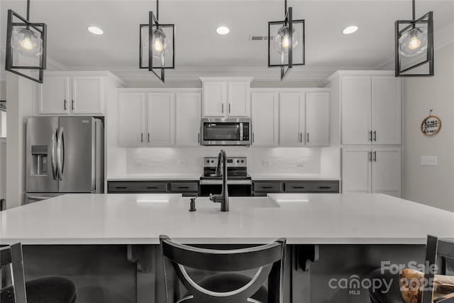 kitchen with white cabinets, ornamental molding, stainless steel appliances, a large island with sink, and a sink