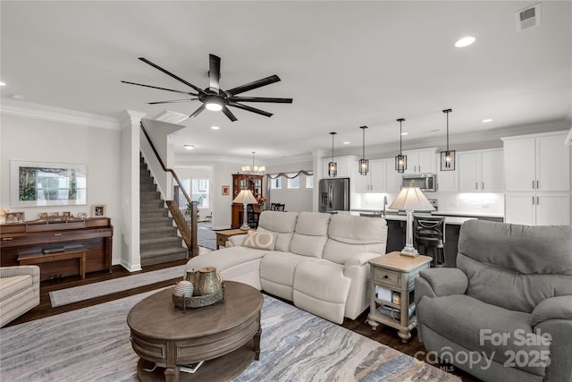 living area featuring a notable chandelier, crown molding, visible vents, wood finished floors, and stairs