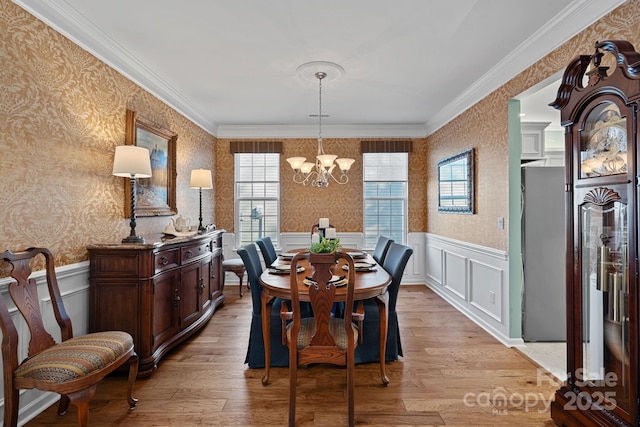 dining area featuring wallpapered walls, light wood finished floors, an inviting chandelier, and wainscoting