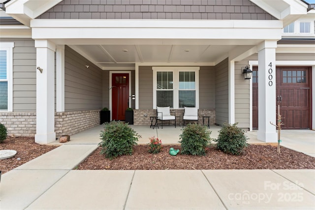 entrance to property featuring a garage, covered porch, and brick siding