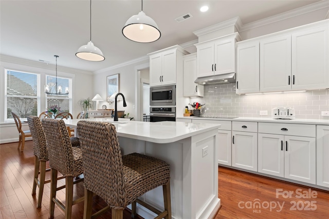 kitchen with a kitchen breakfast bar, appliances with stainless steel finishes, ornamental molding, and under cabinet range hood