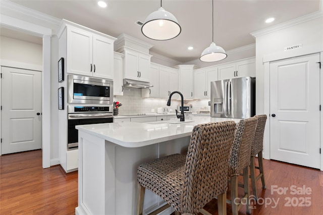 kitchen with stainless steel appliances, a breakfast bar, crown molding, and under cabinet range hood