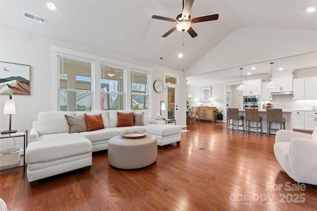 living area with high vaulted ceiling, ceiling fan, visible vents, and dark wood-type flooring