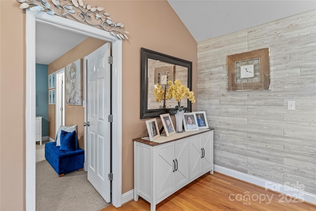 hall with wood walls, an accent wall, baseboards, and vaulted ceiling