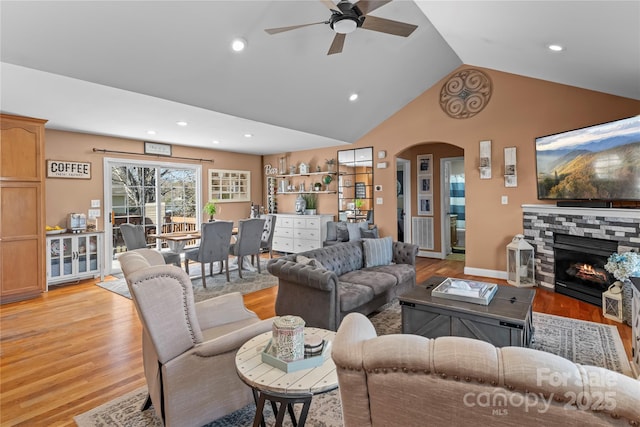 living room featuring arched walkways, lofted ceiling, light wood-style flooring, recessed lighting, and a fireplace