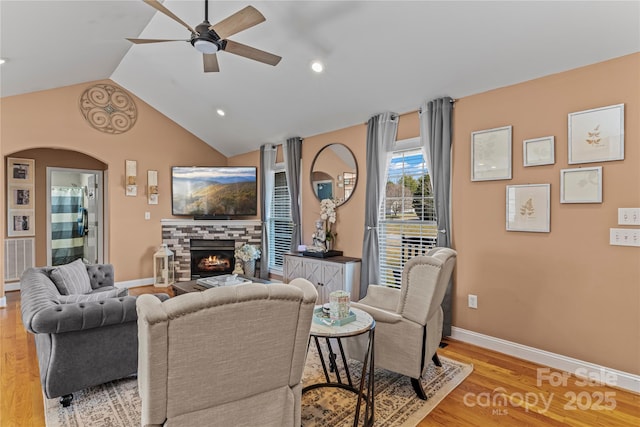 living room with arched walkways, a fireplace, vaulted ceiling, light wood-type flooring, and baseboards