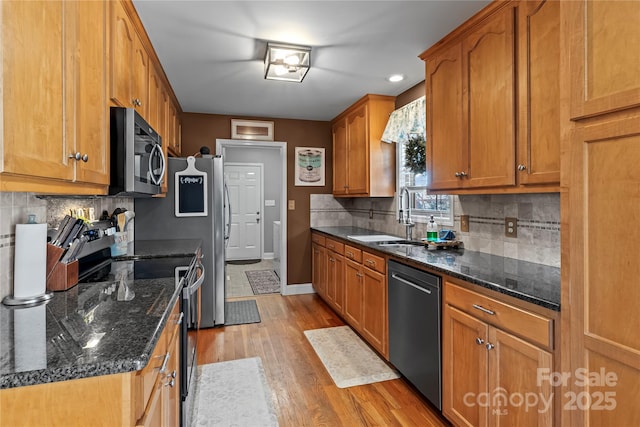 kitchen with stainless steel appliances, light wood-style flooring, brown cabinetry, a sink, and baseboards