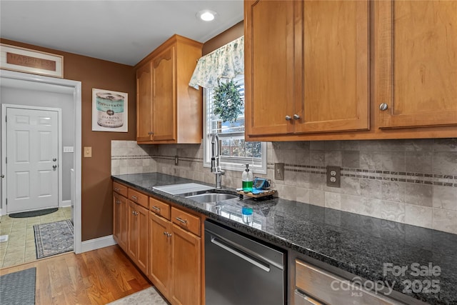 kitchen featuring a sink, baseboards, stainless steel dishwasher, backsplash, and dark stone counters