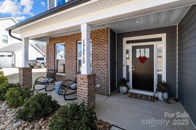 view of exterior entry featuring a porch and brick siding