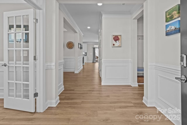 hall with crown molding, recessed lighting, a decorative wall, light wood-style flooring, and wainscoting