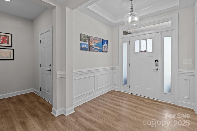 entryway with a wainscoted wall, light wood finished floors, a raised ceiling, and a decorative wall