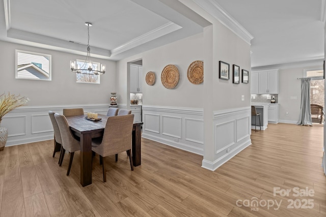 dining area with an inviting chandelier, a tray ceiling, crown molding, light wood-style floors, and a decorative wall