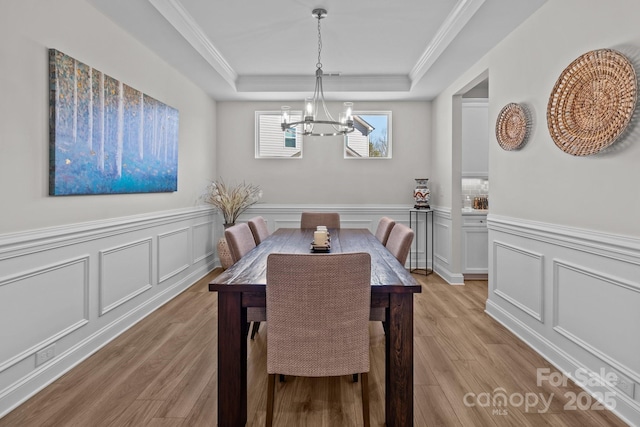 dining space featuring light wood finished floors, a tray ceiling, ornamental molding, and an inviting chandelier