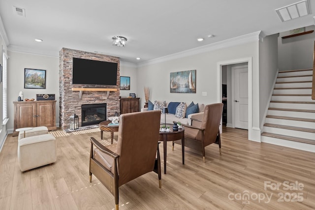 living area with ornamental molding, light wood-type flooring, a fireplace, and stairs