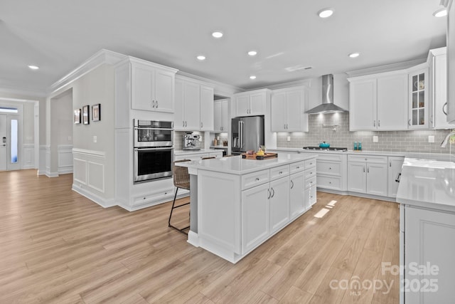 kitchen with stainless steel appliances, white cabinets, light countertops, wall chimney exhaust hood, and glass insert cabinets