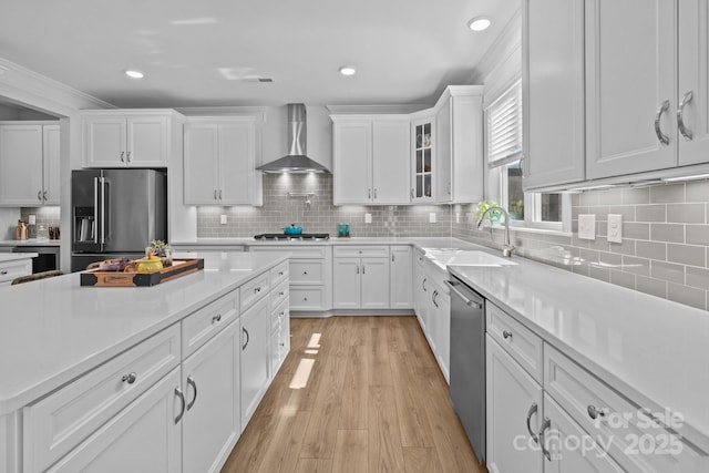 kitchen with wall chimney exhaust hood, glass insert cabinets, appliances with stainless steel finishes, light countertops, and a sink