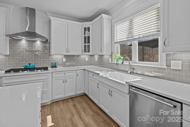 kitchen with stainless steel appliances, light countertops, white cabinets, a sink, and wall chimney exhaust hood