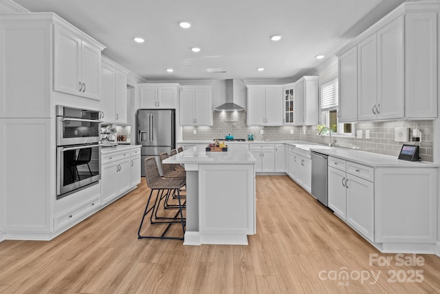 kitchen with a kitchen island, white cabinetry, light countertops, appliances with stainless steel finishes, and wall chimney exhaust hood