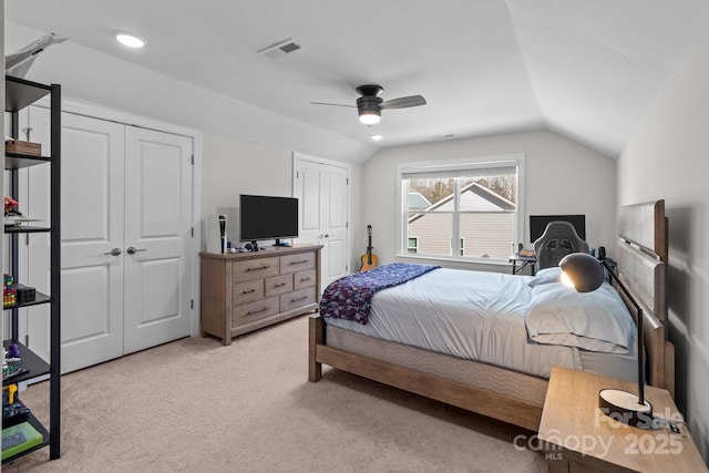 bedroom featuring visible vents, a ceiling fan, light colored carpet, lofted ceiling, and multiple closets