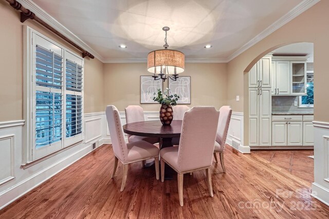 dining space featuring a decorative wall, arched walkways, light wood finished floors, and ornamental molding