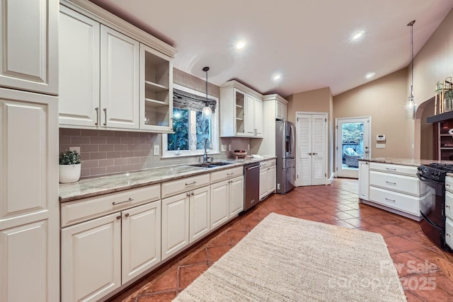 kitchen with pendant lighting, a sink, appliances with stainless steel finishes, glass insert cabinets, and vaulted ceiling