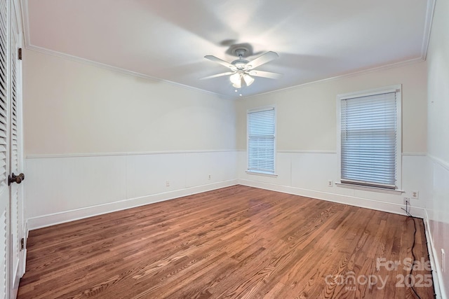 unfurnished room featuring a wainscoted wall, a ceiling fan, wood finished floors, and crown molding