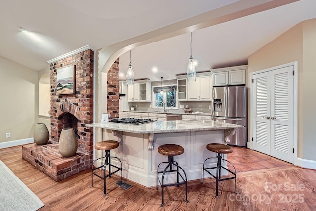 kitchen with glass insert cabinets, a breakfast bar area, light stone counters, stainless steel appliances, and a sink