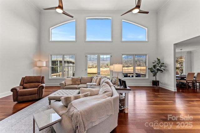 living area featuring ceiling fan with notable chandelier, dark wood-style flooring, baseboards, and crown molding