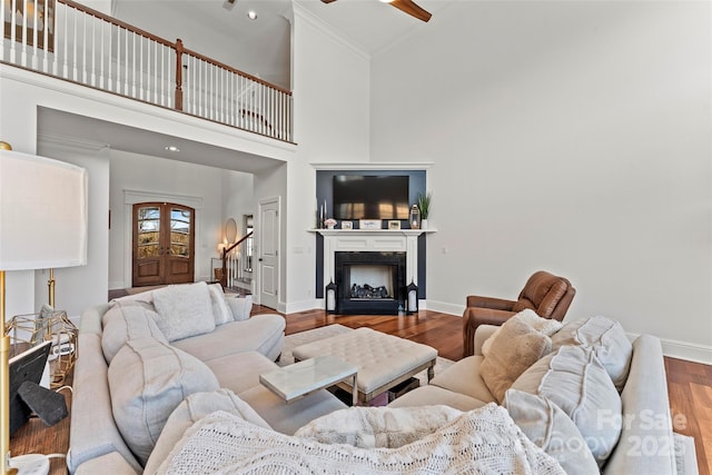 living area featuring a fireplace, a towering ceiling, baseboards, and wood finished floors