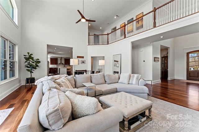 living room featuring crown molding, a high ceiling, baseboards, and wood finished floors