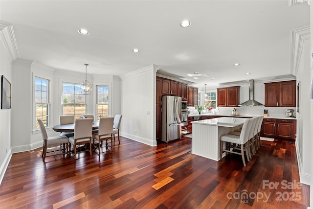 kitchen featuring freestanding refrigerator, a center island, an inviting chandelier, light countertops, and wall chimney range hood