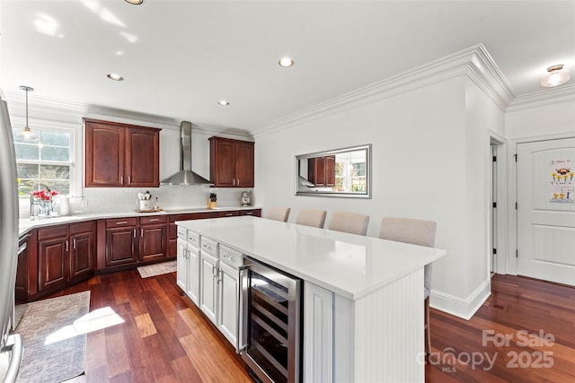 kitchen featuring wine cooler, light countertops, a center island, wall chimney exhaust hood, and decorative light fixtures