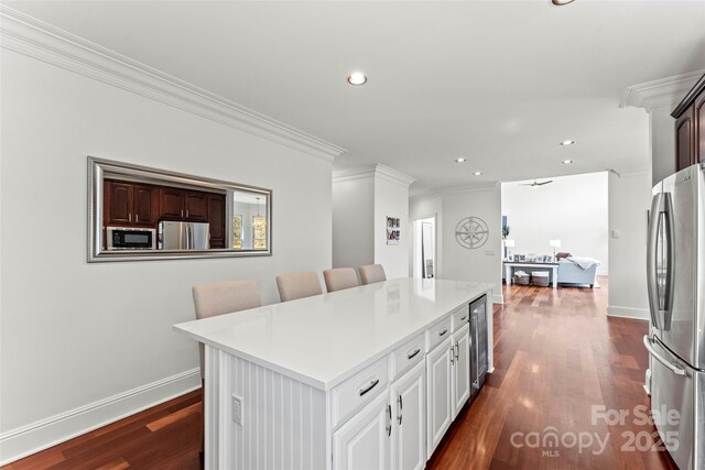 kitchen with white cabinets, a kitchen island, a breakfast bar, freestanding refrigerator, and black microwave