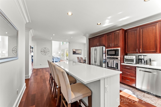 kitchen with appliances with stainless steel finishes, light countertops, a breakfast bar area, and ornamental molding