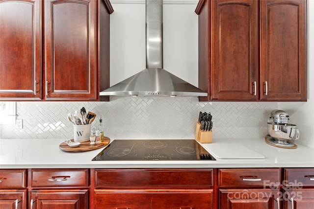 kitchen featuring reddish brown cabinets, light countertops, wall chimney exhaust hood, and black electric cooktop