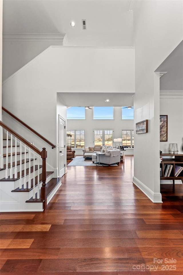 entryway with dark wood finished floors, crown molding, and stairs