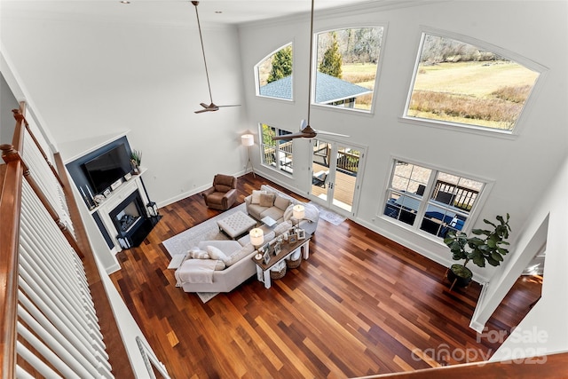 living area featuring dark wood-style flooring, a fireplace, a towering ceiling, baseboards, and a ceiling fan