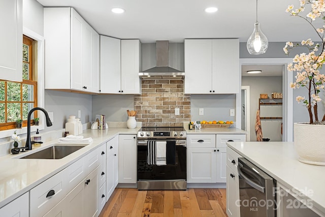 kitchen with stainless steel appliances, light countertops, a sink, light wood-type flooring, and wall chimney exhaust hood