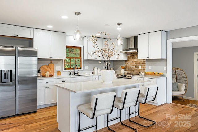 kitchen featuring wall chimney exhaust hood, light wood-style flooring, appliances with stainless steel finishes, white cabinetry, and a sink