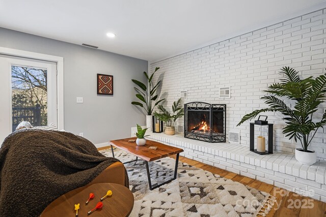 living area with baseboards, brick wall, wood finished floors, a brick fireplace, and recessed lighting