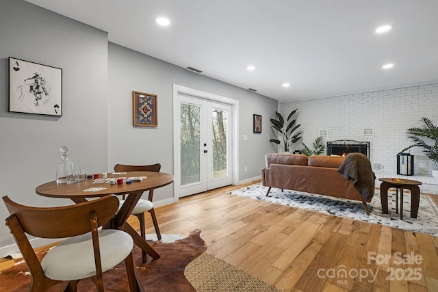 living room with french doors, light wood finished floors, recessed lighting, a brick fireplace, and brick wall