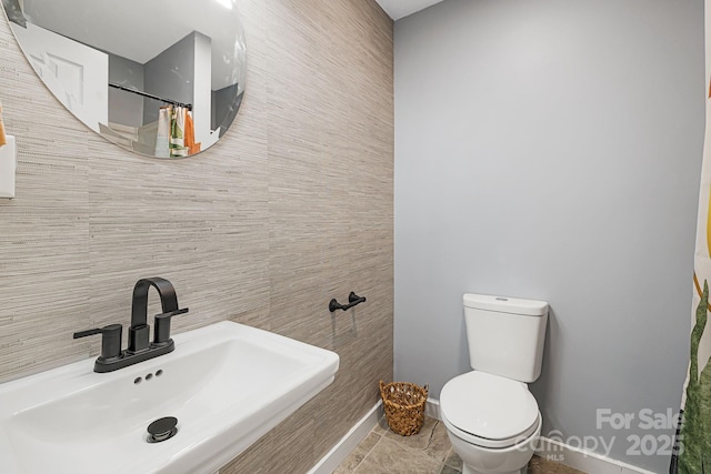 bathroom featuring baseboards, toilet, a shower with curtain, a sink, and tile walls